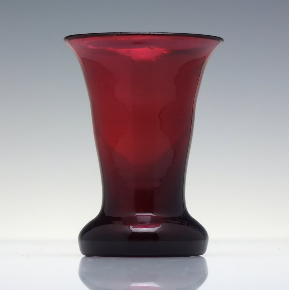 A small Victorian ruby glass dram tumbler with a flared lip and heavy thick base against a plain background. View II