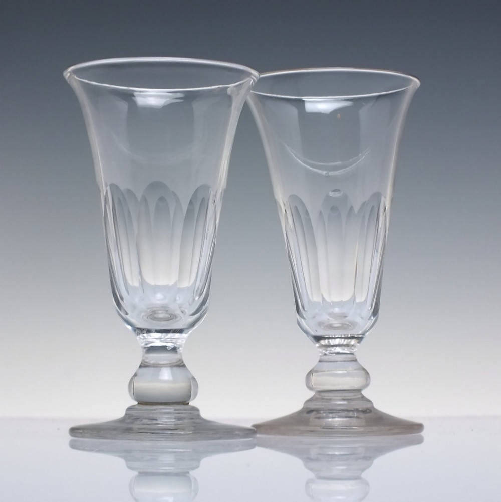 A pair of clear cut-glass Georgian jelly glasses featuring flared rims, panel-cut lower bowls, short knopped stems, and circular flat bases.