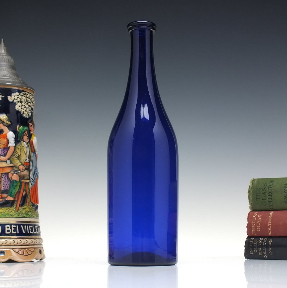 A dark cobalt blue Victorian hand-blown glass serving bottle featuring a tapered neck, double collar, and smooth cylindrical body.