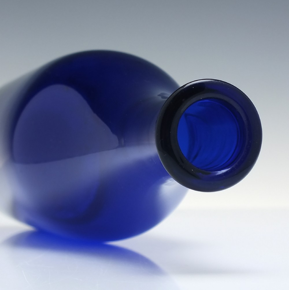 A dark cobalt blue Victorian hand-blown glass serving bottle featuring a tapered neck, double collar, and smooth cylindrical body. View IV