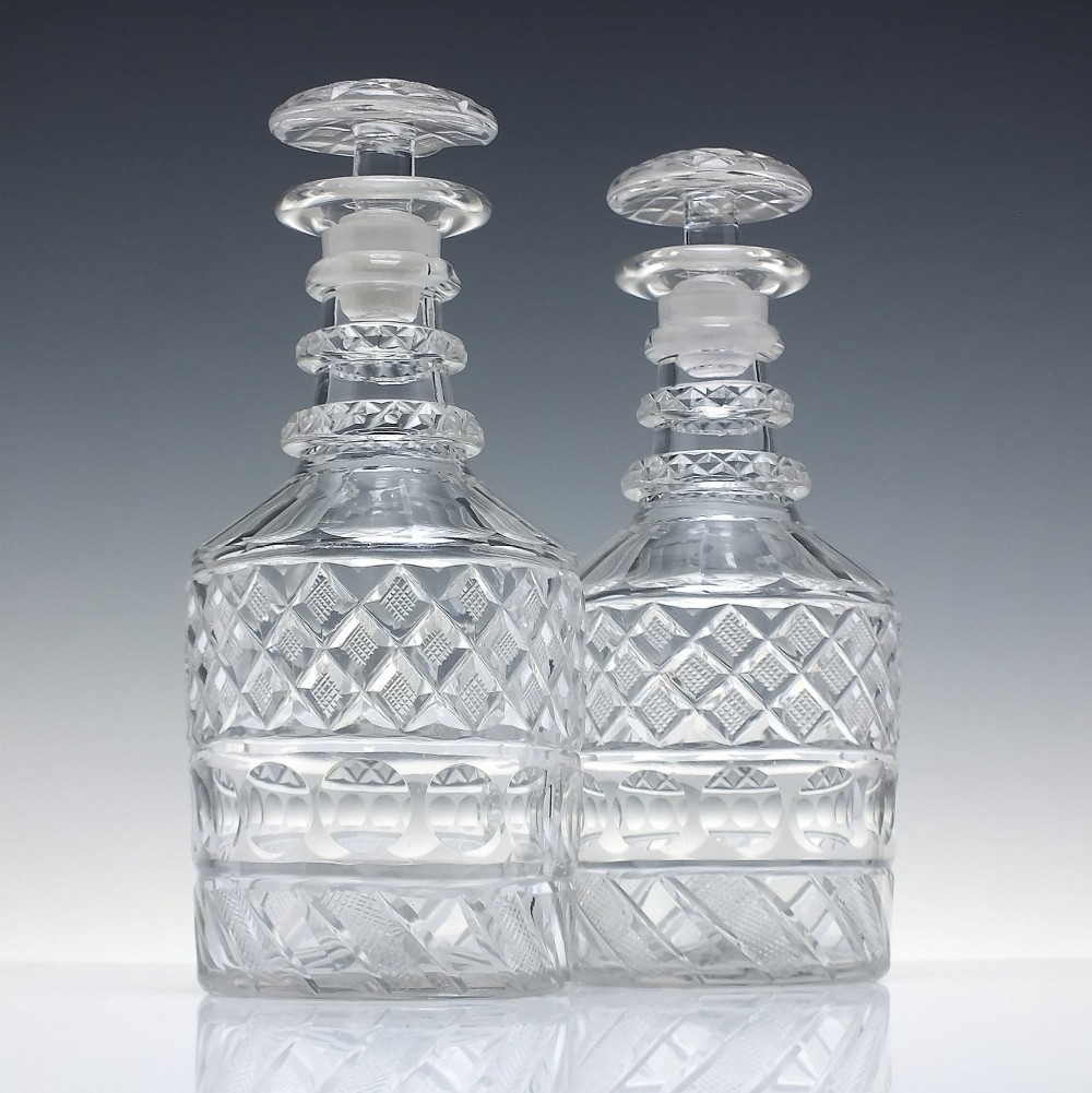 A pair of clear cut lead crystal Georgian decanters featuring diamond cut bands, neck rings, and mushroom stoppers.