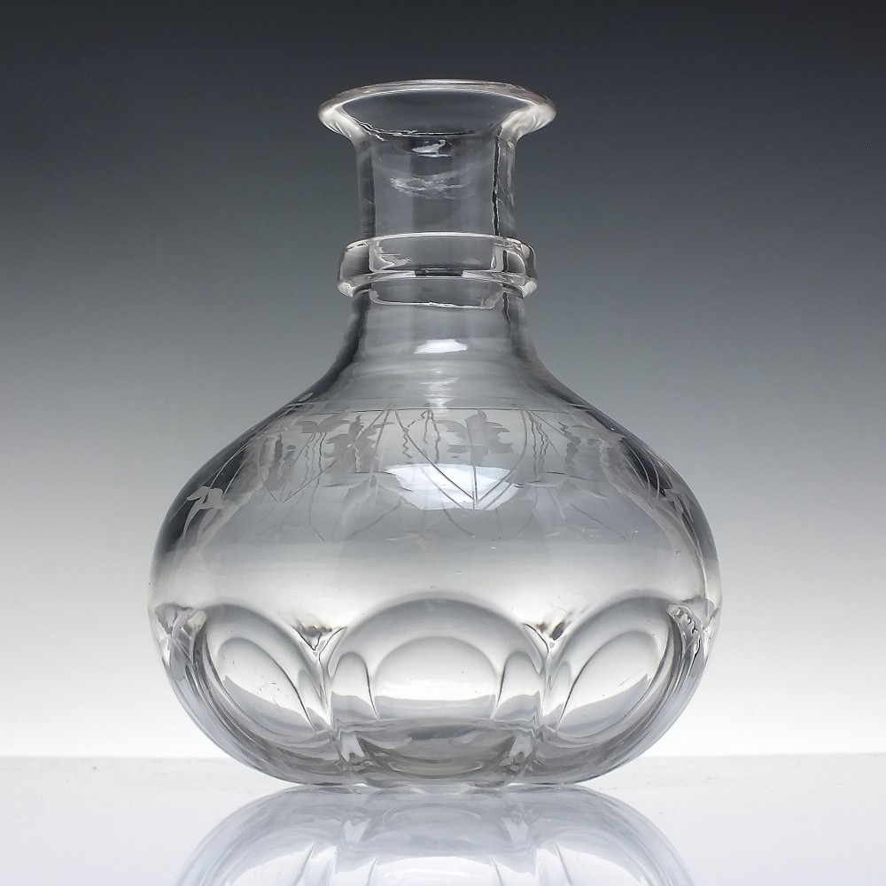 A mid-19th century clear glass wine carafe featuring an engraved foliate upper band and cut panel arches around the bulbous base.