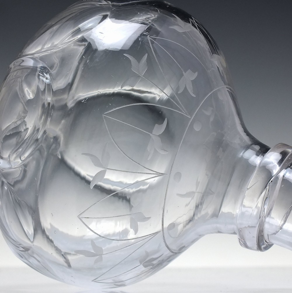 A mid-19th century clear glass wine carafe featuring an engraved foliate upper band and cut panel arches around the bulbous base. View IV