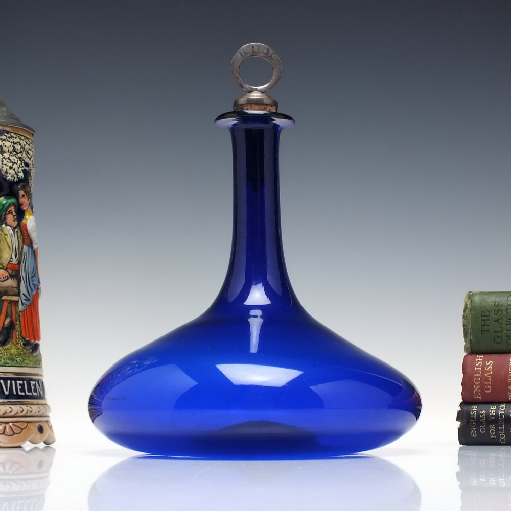 A Georgian cobalt blue glass mell decanter with a wide rounded base, narrow neck, and a cork stopper with a metal ring labeled RUM.