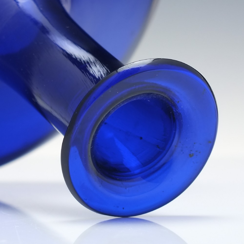 A Georgian cobalt blue glass mell decanter with a wide rounded base, narrow neck, and a cork stopper with a metal ring labeled RUM. View IV