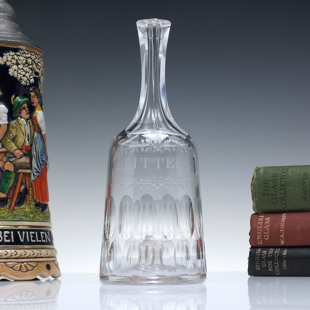 An 18th-century clear glass sugar loaf bitters bottle featuring a faceted slender neck, cut panel base, and wheel-engraved lettering spelling BITTERS surrounded by floral swags.