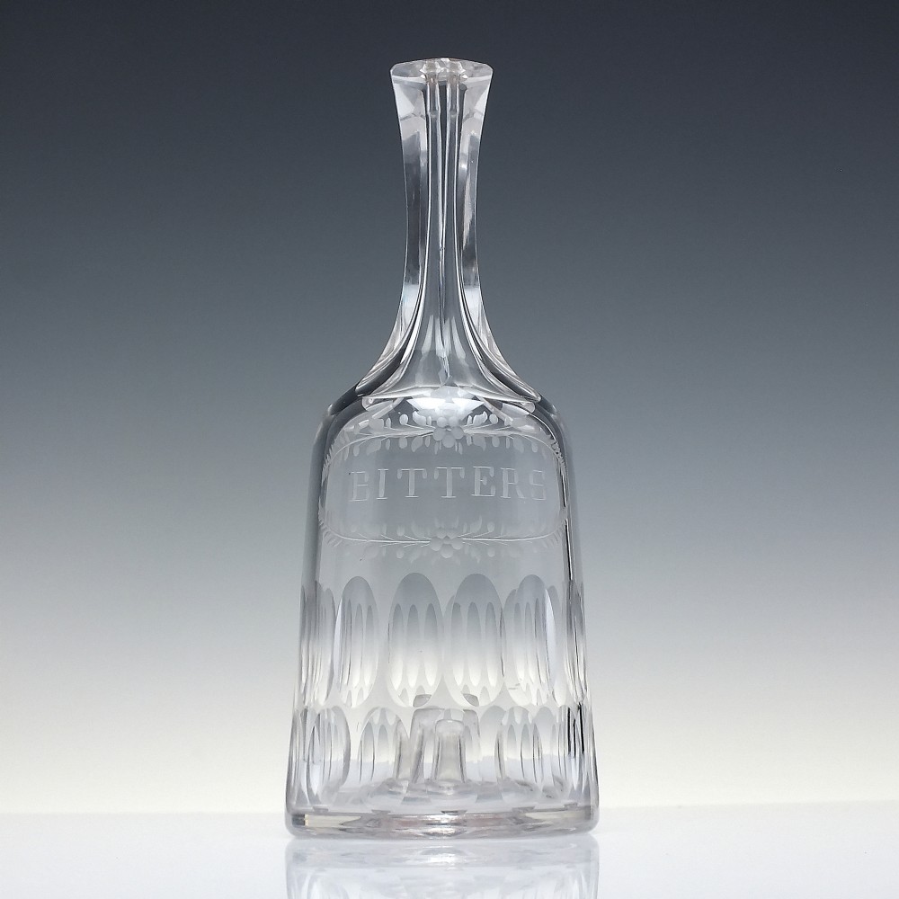 An 18th-century clear glass sugar loaf bitters bottle featuring a faceted slender neck, cut panel base, and wheel-engraved lettering spelling BITTERS surrounded by floral swags. View II