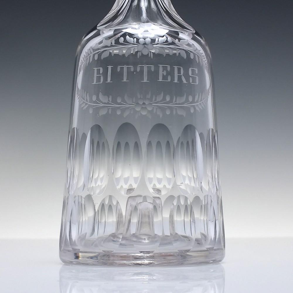 An 18th-century clear glass sugar loaf bitters bottle featuring a faceted slender neck, cut panel base, and wheel-engraved lettering spelling BITTERS surrounded by floral swags. View IV