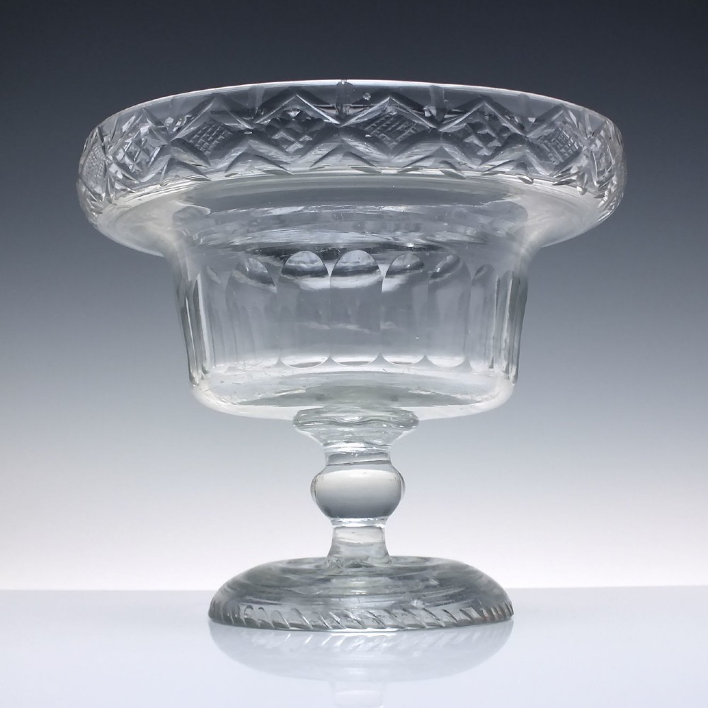 A clear Georgian cut glass standing bowl featuring a wide diamond-cut rim, fluted basin, knopped stem, and circular foot.