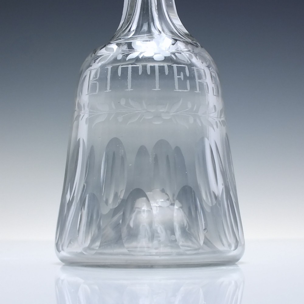 A pair of 18th-century clear glass sugar loaf bitters bottles featuring facet-cut long necks, hand-engraved floral garlands, and the word BITTERS cut into the body. View V