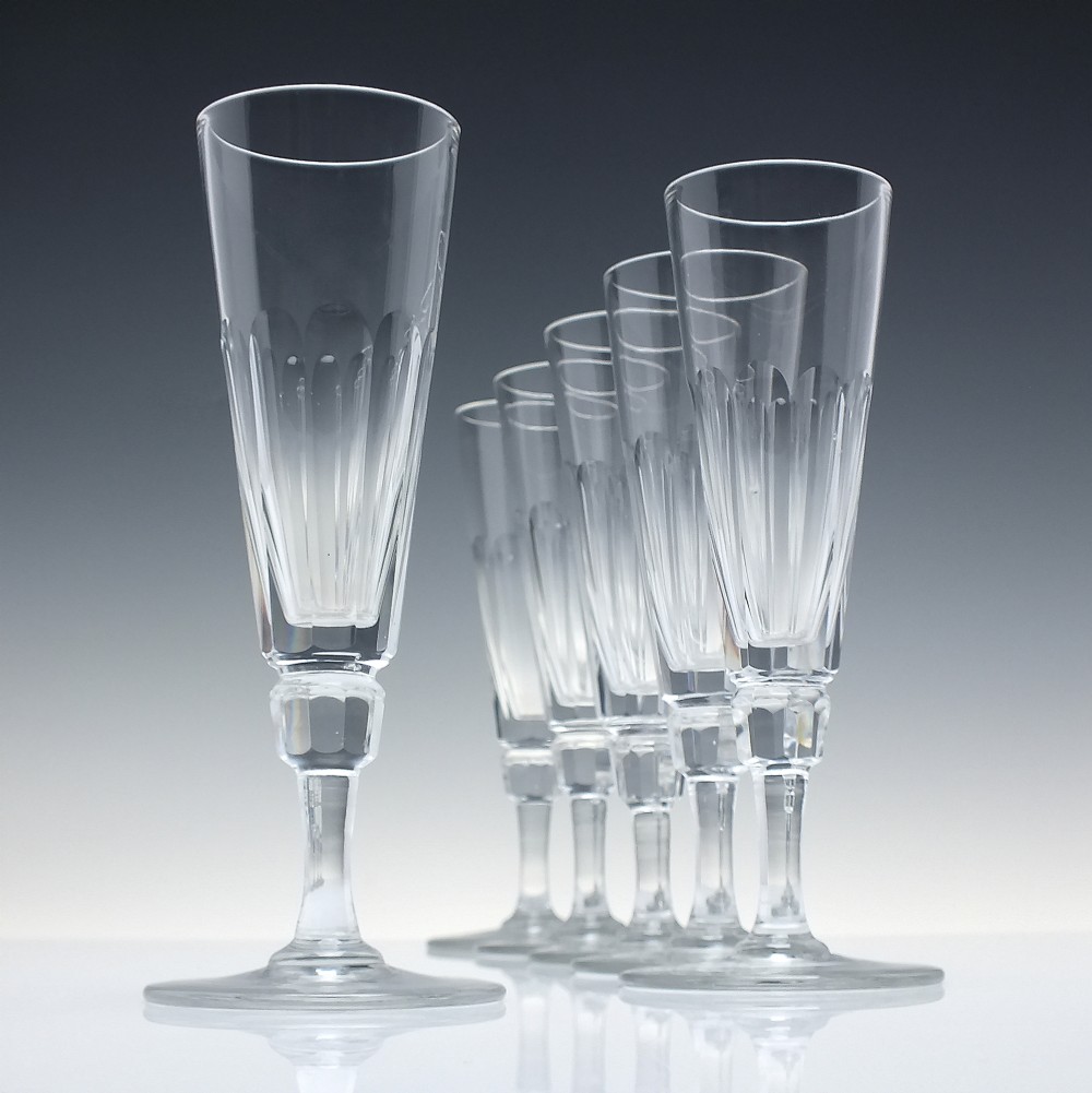 A set of six Victorian clear cut glass champagne flutes arranged in a row, featuring tall conical bowls with basal panel cutting and faceted stems.