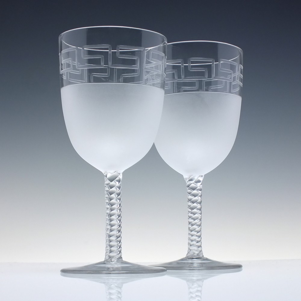 A pair of clear and frosted Edwardian glass wine goblets featuring a Greek key engraved border and spiral twisted stems.
