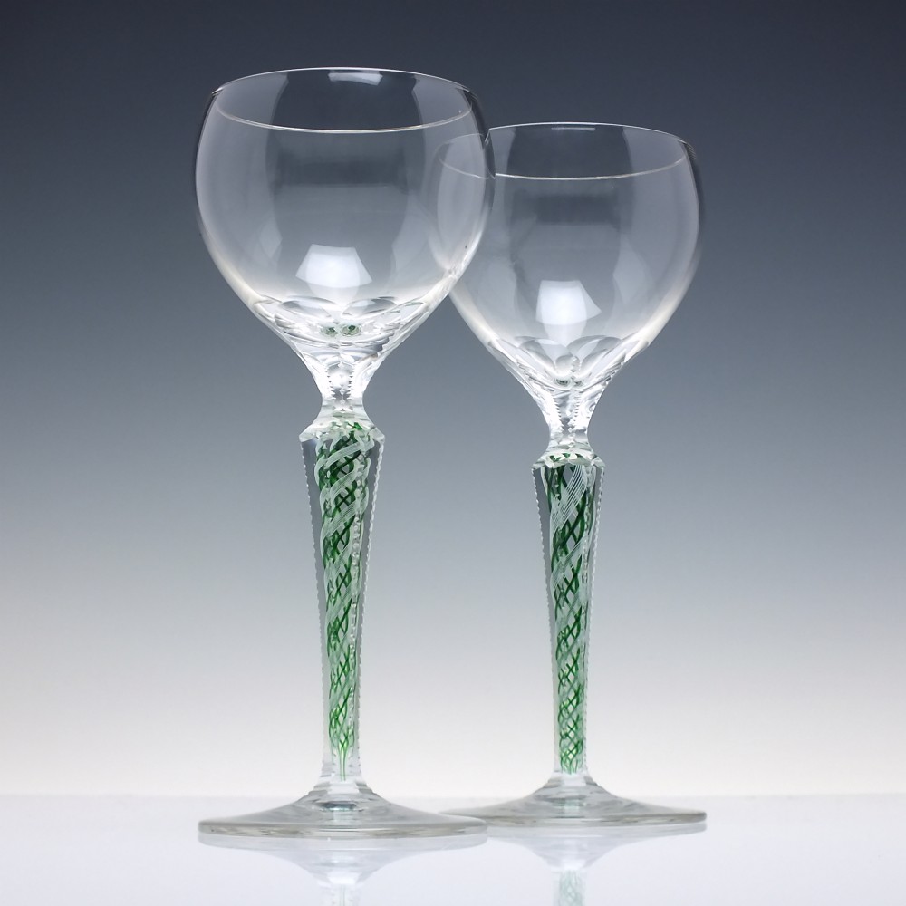 A pair of clear glass wine goblets featuring round bowls and tall stems decorated with internal green and white opaque twists.