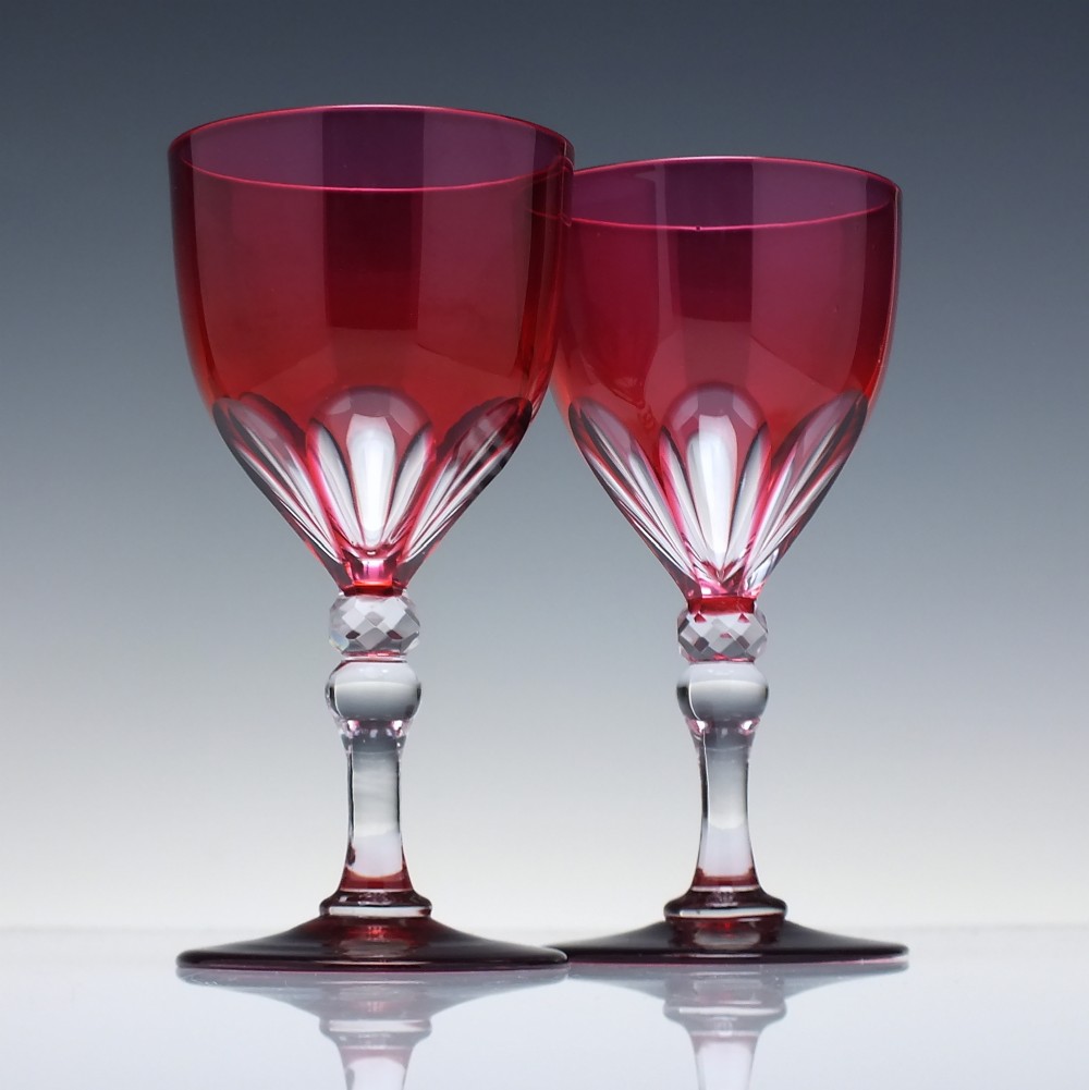 A line of six Victorian cranberry glass wine goblets featuring cut-to-clear patterned bases and faceted clear stems. View II