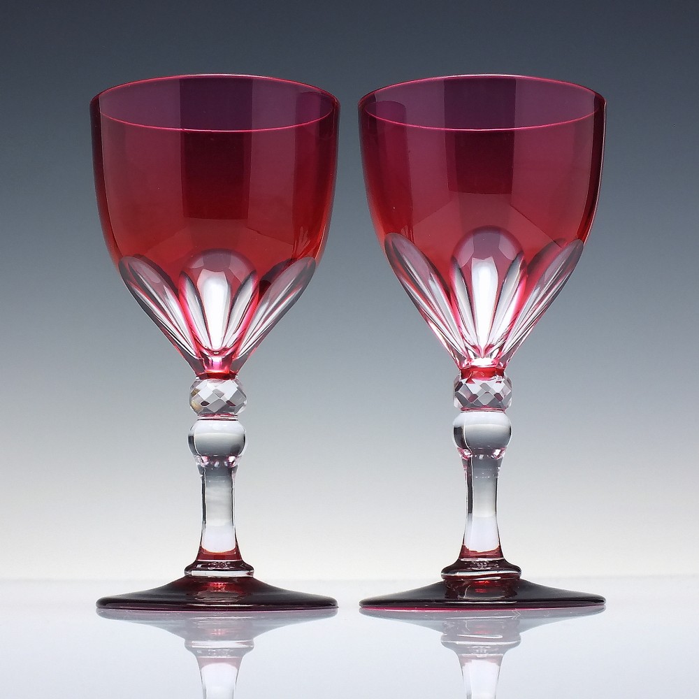 A line of six Victorian cranberry glass wine goblets featuring cut-to-clear patterned bases and faceted clear stems. View III