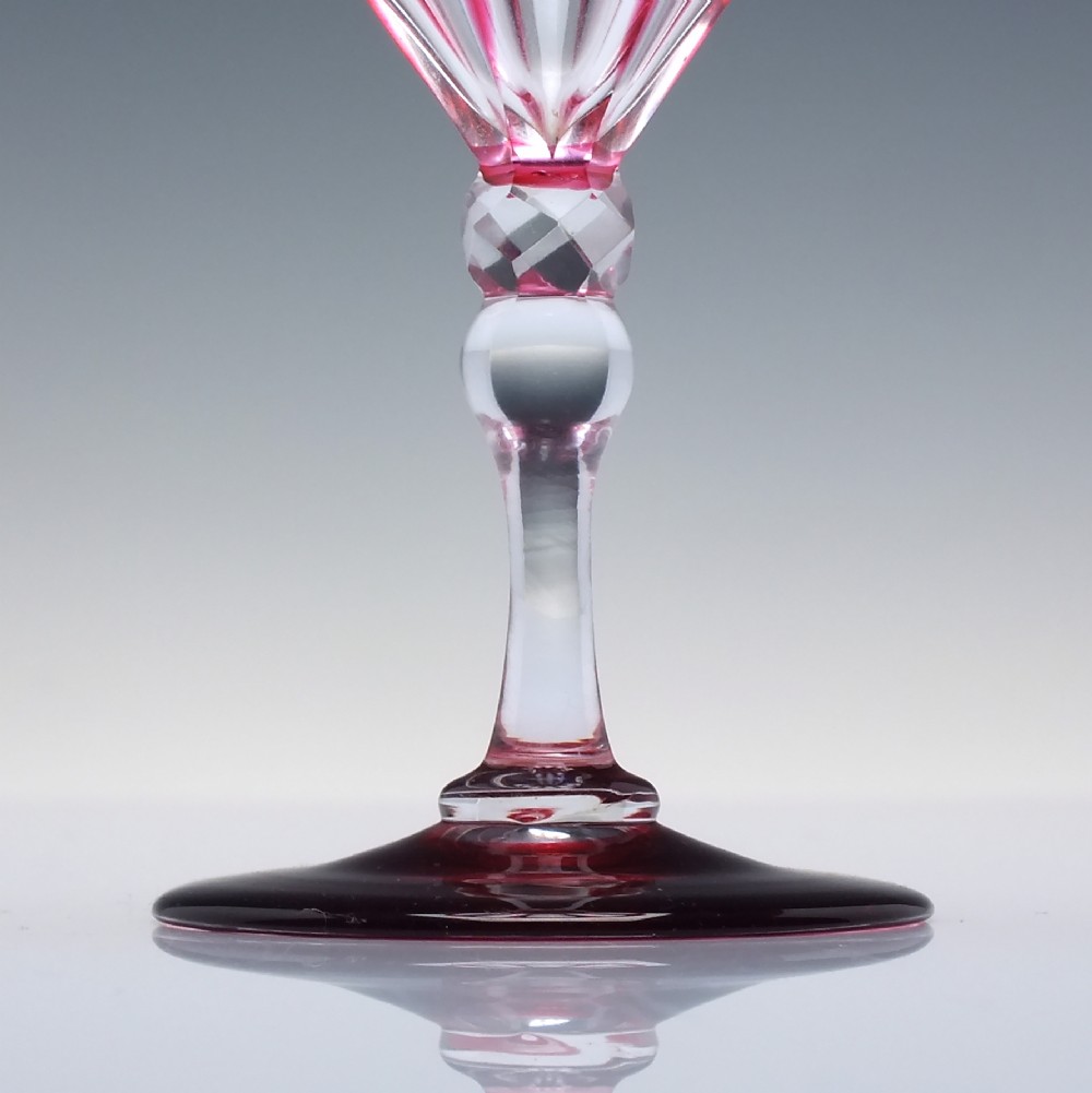 A line of six Victorian cranberry glass wine goblets featuring cut-to-clear patterned bases and faceted clear stems. View IV