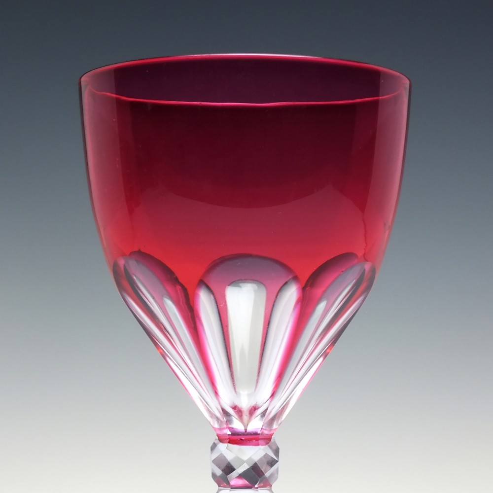 A line of six Victorian cranberry glass wine goblets featuring cut-to-clear patterned bases and faceted clear stems. View V