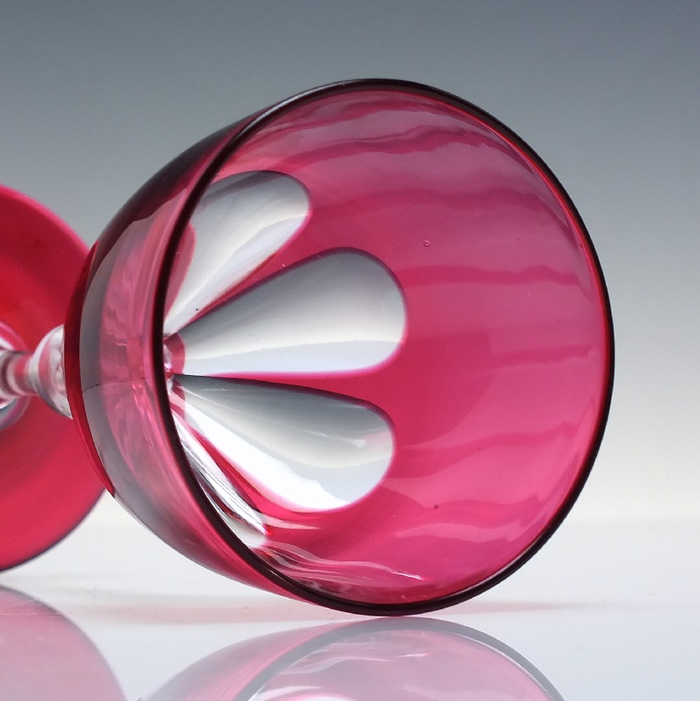 A line of six Victorian cranberry glass wine goblets featuring cut-to-clear patterned bases and faceted clear stems. View VI