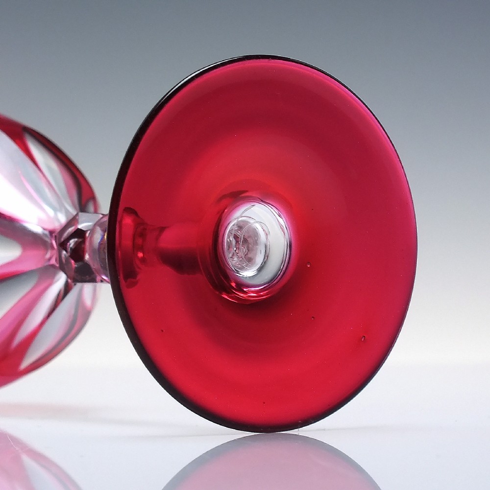 A line of six Victorian cranberry glass wine goblets featuring cut-to-clear patterned bases and faceted clear stems. View VII
