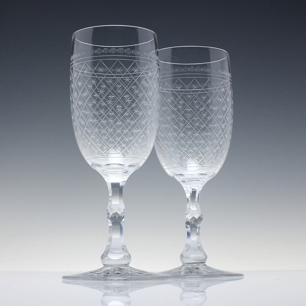 A pair of clear glass Victorian wine goblets featuring star and diamond pattern engravings with faceted stems.