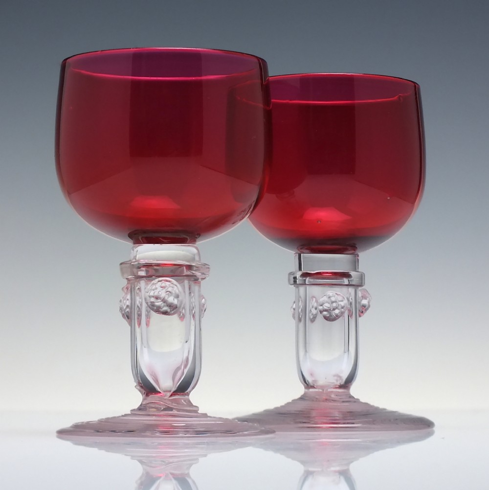 A pair of nineteenth-century Victorian wine glasses featuring deep cranberry red bowls and clear glass stems decorated with applied raspberry prunts.