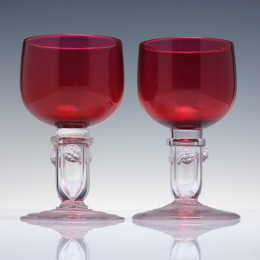 A pair of nineteenth-century Victorian wine glasses featuring deep cranberry red bowls and clear glass stems decorated with applied raspberry prunts. View II