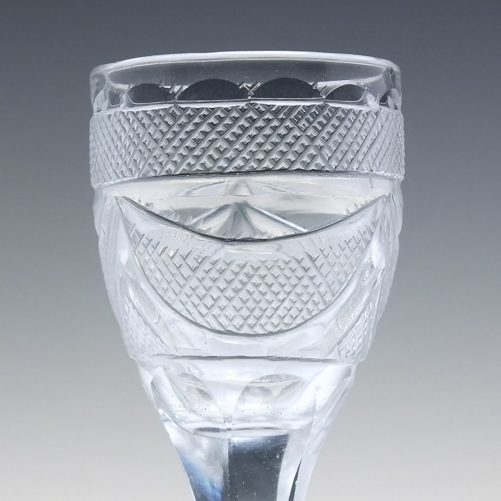An antique clear cut lead crystal dram glass featuring diamond lattice cutting on the bowl, a faceted stem, and a flat circular base. View VI