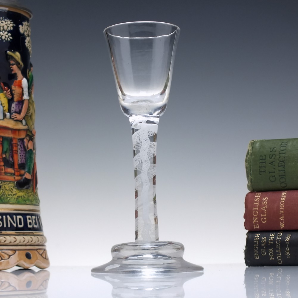 A clear Georgian lead glass wine glass featuring an internal white opaque twist stem and a stepped helmet foot.