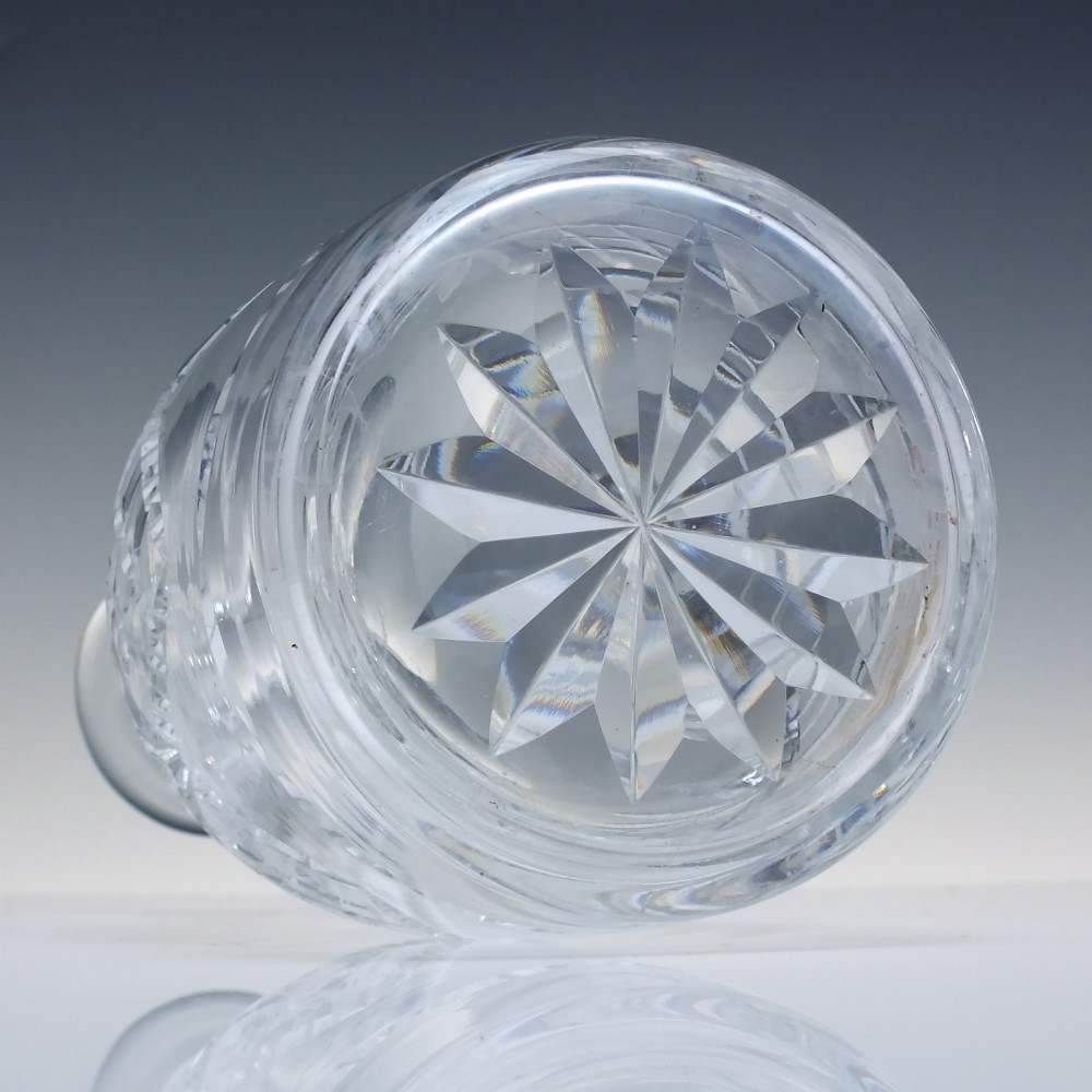 A clear cut crystal glass decanter with a geometric diamond cut body, smooth neck, and faceted glass stopper. View V