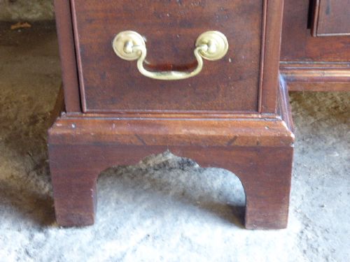 An antique Georgian mahogany kneehole desk featuring brass swan-neck handles, a central recessed cupboard, and bracket feet. View V