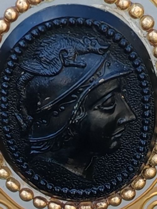 A white opaline glass vase featuring a slender neck, a pedestal base, gold filigree detailing, and a black classical profile cameo medallion at the centre. View IV