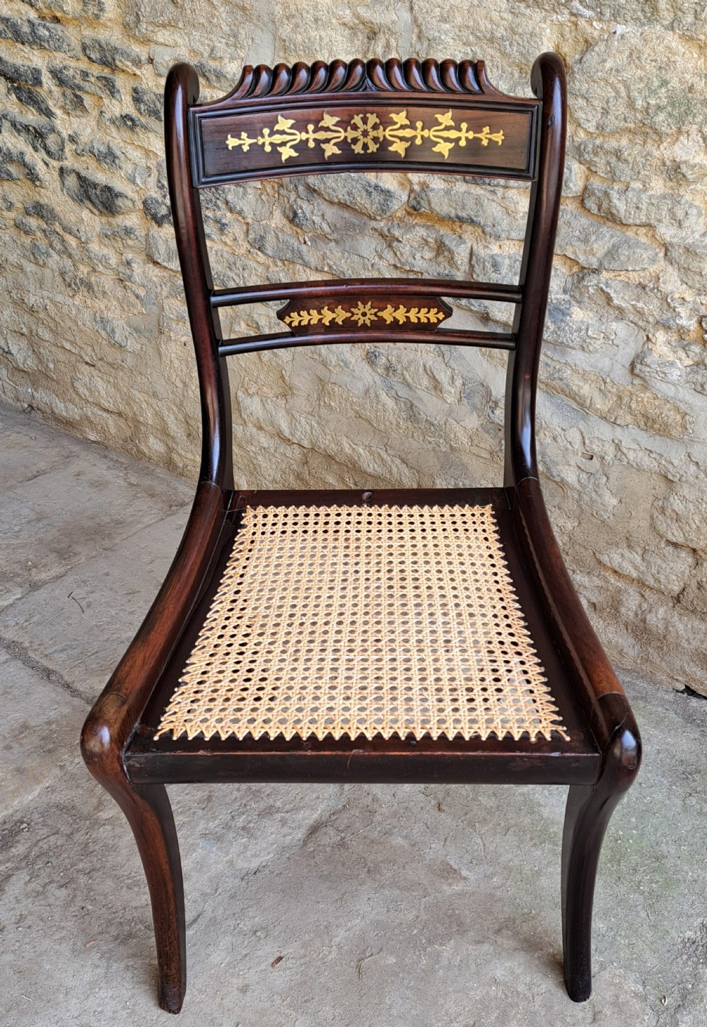 A set of four Regency period rosewood side chairs featuring intricate brass scrollwork inlay on the backrests, woven cane seats, and curved sabre legs. View III