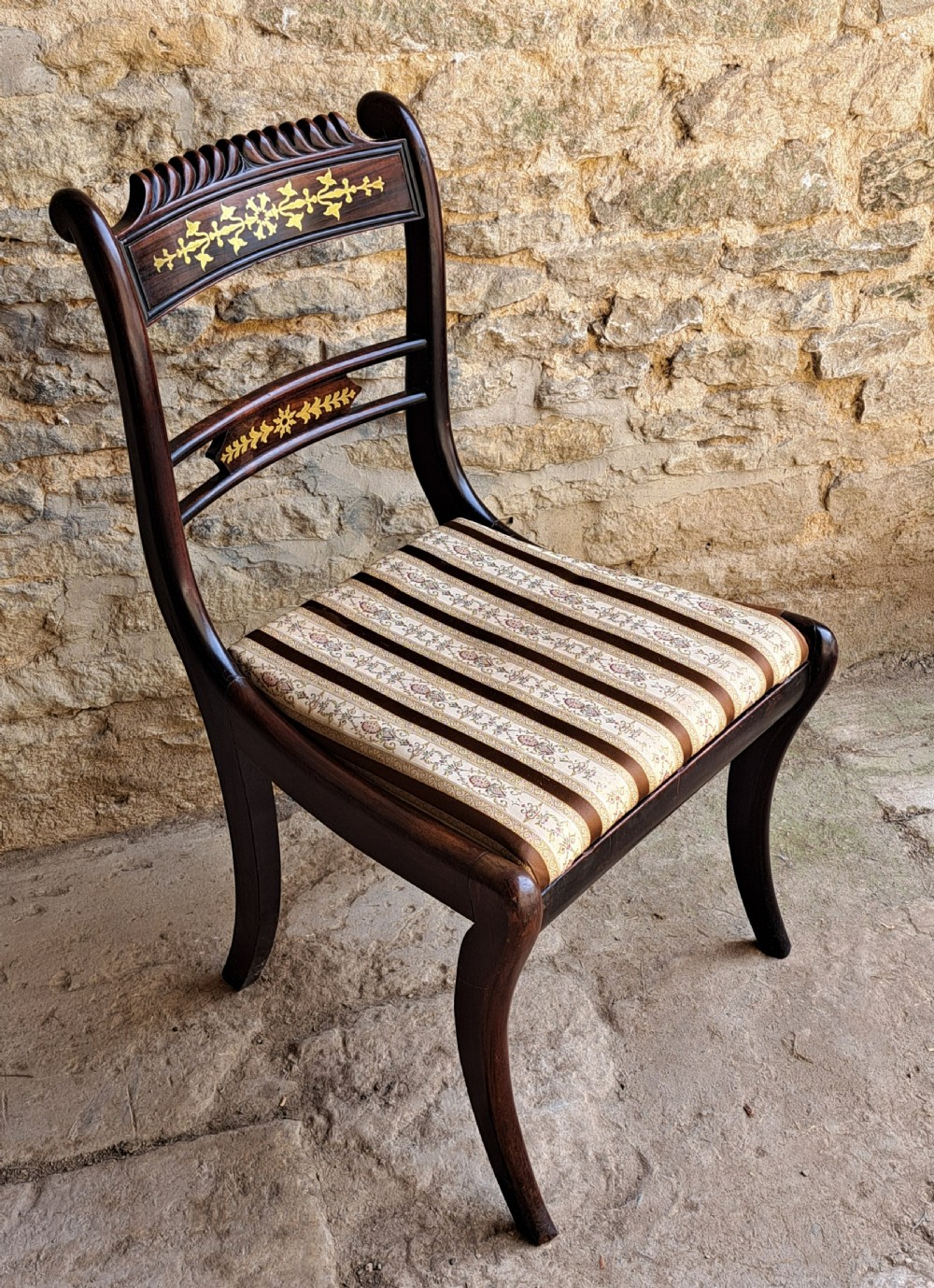 A set of four Regency period rosewood side chairs featuring intricate brass scrollwork inlay on the backrests, woven cane seats, and curved sabre legs. View IX
