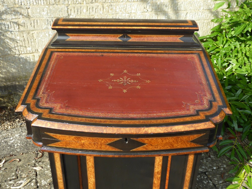 An ebonised and amboyna wood Davenport desk featuring a slanted red leather writing surface, geometric inlay, and an open side door revealing four drawers. View V