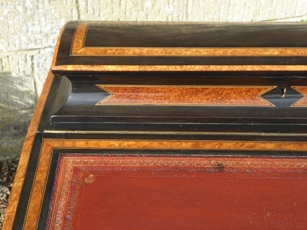 An ebonised and amboyna wood Davenport desk featuring a slanted red leather writing surface, geometric inlay, and an open side door revealing four drawers. View VI