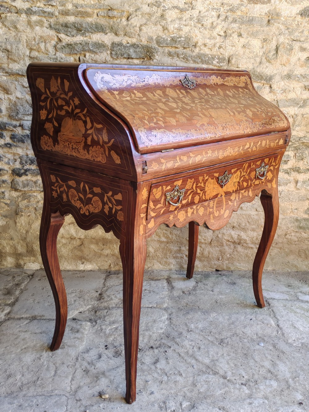 An antique Dutch mahogany writing bureau with intricate floral wood marquetry, a sloped fall front, a single drawer, and cabriole legs.