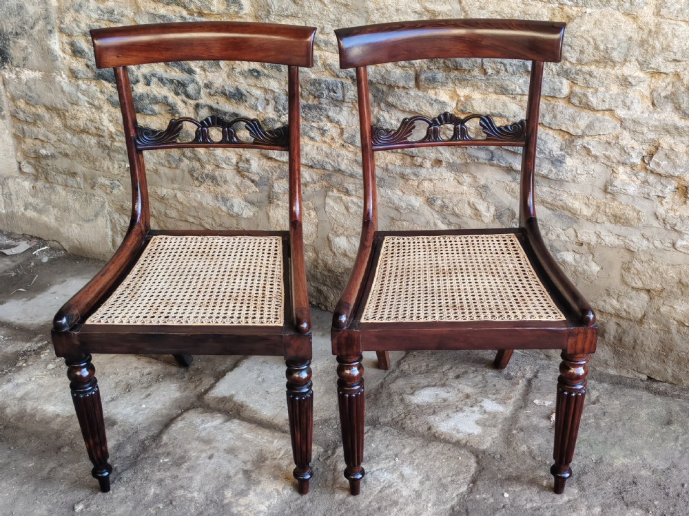A pair of circa 1830 rosewood dining chairs featuring carved back splats, woven cane seats, and reeded front legs.