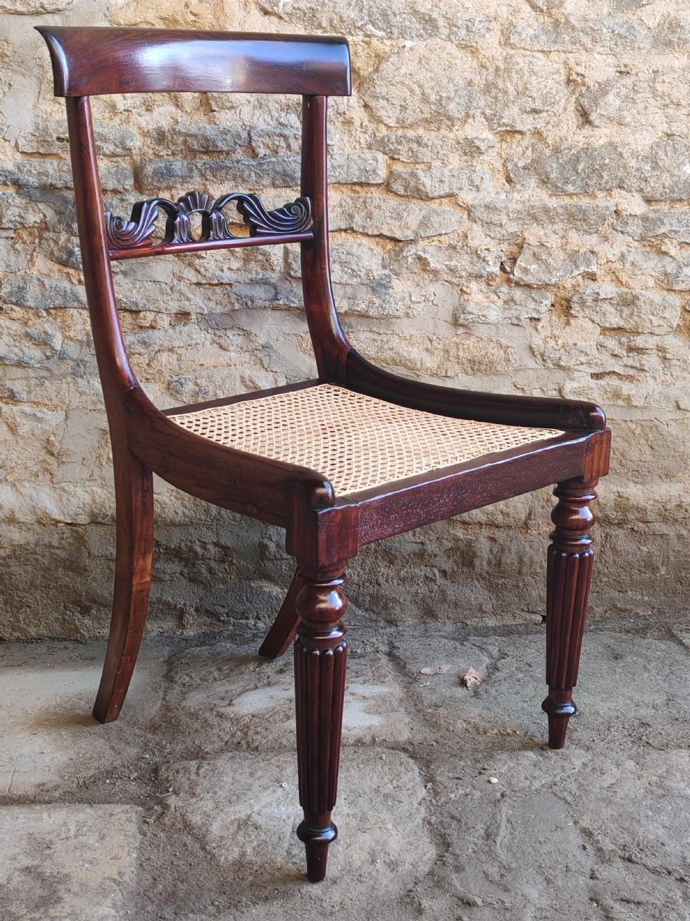 A pair of circa 1830 rosewood dining chairs featuring carved back splats, woven cane seats, and reeded front legs. View II