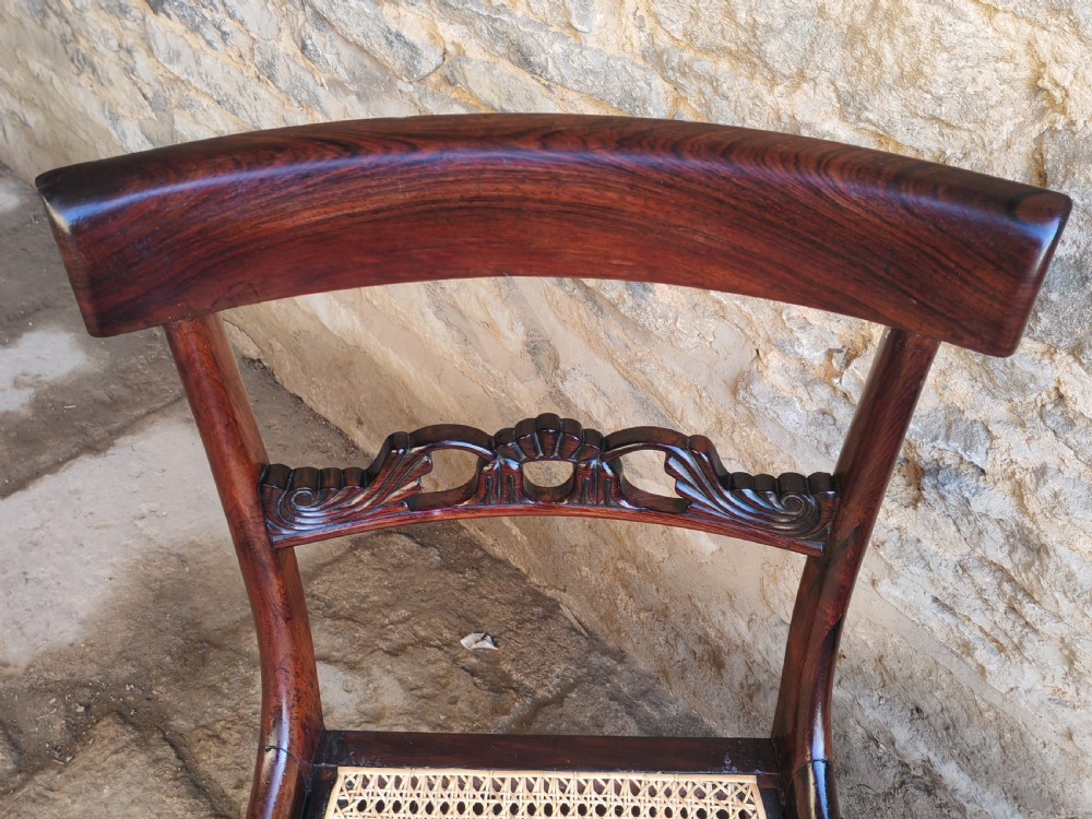 A pair of circa 1830 rosewood dining chairs featuring carved back splats, woven cane seats, and reeded front legs. View IV