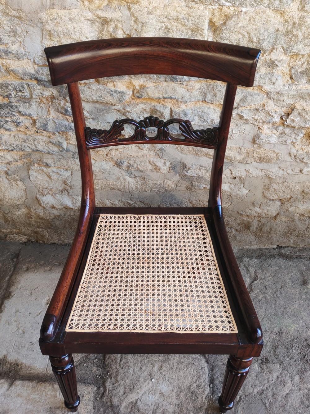A pair of circa 1830 rosewood dining chairs featuring carved back splats, woven cane seats, and reeded front legs. View VI