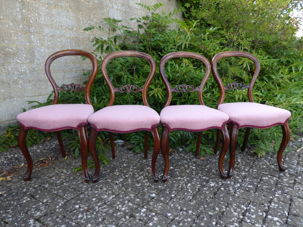 A set of four late Victorian walnut dining chairs featuring balloon backs, carved central splats, cabriole front legs, and pink upholstered seats.
