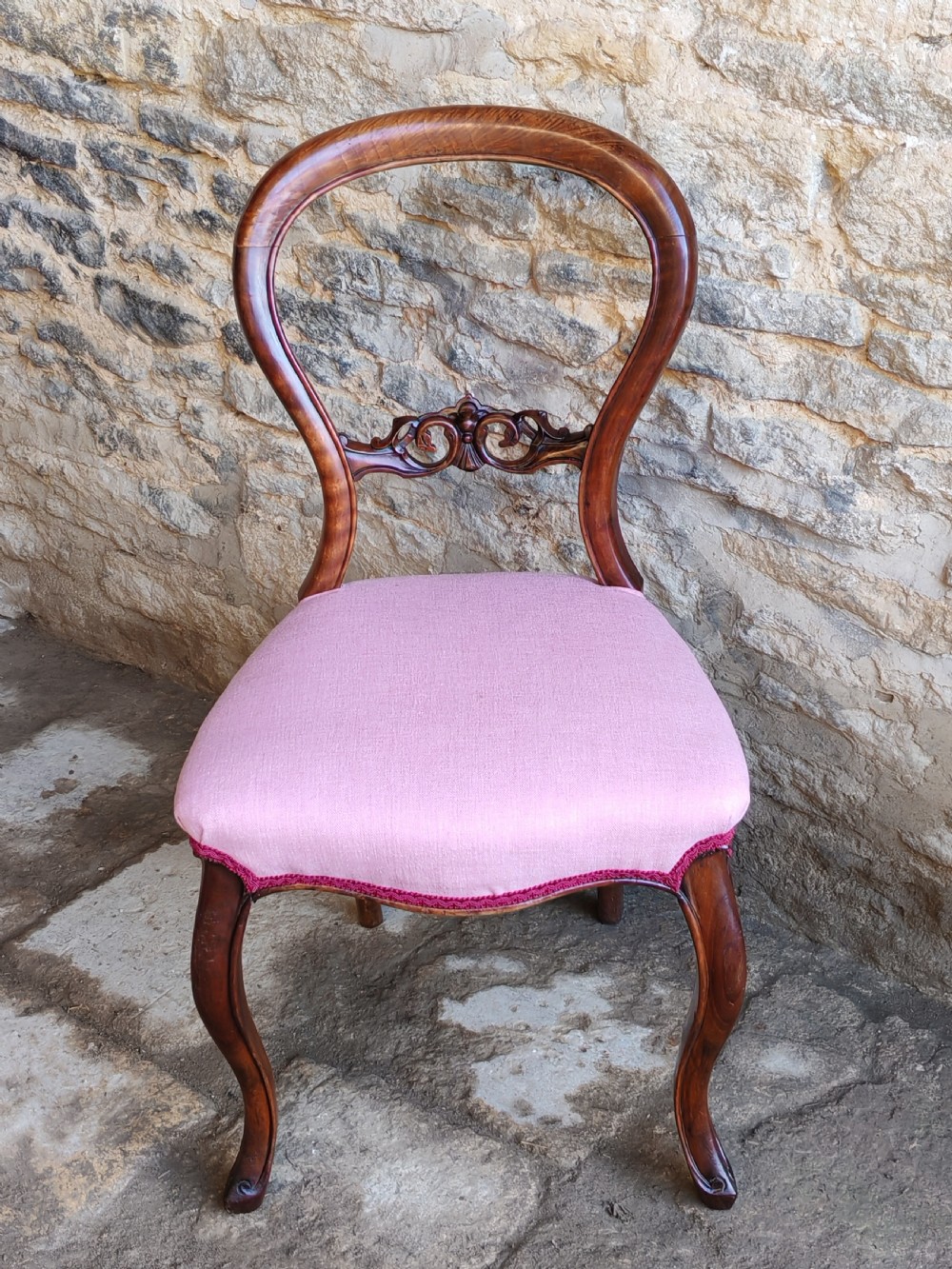 A set of four late Victorian walnut dining chairs featuring balloon backs, carved central splats, cabriole front legs, and pink upholstered seats. View IV
