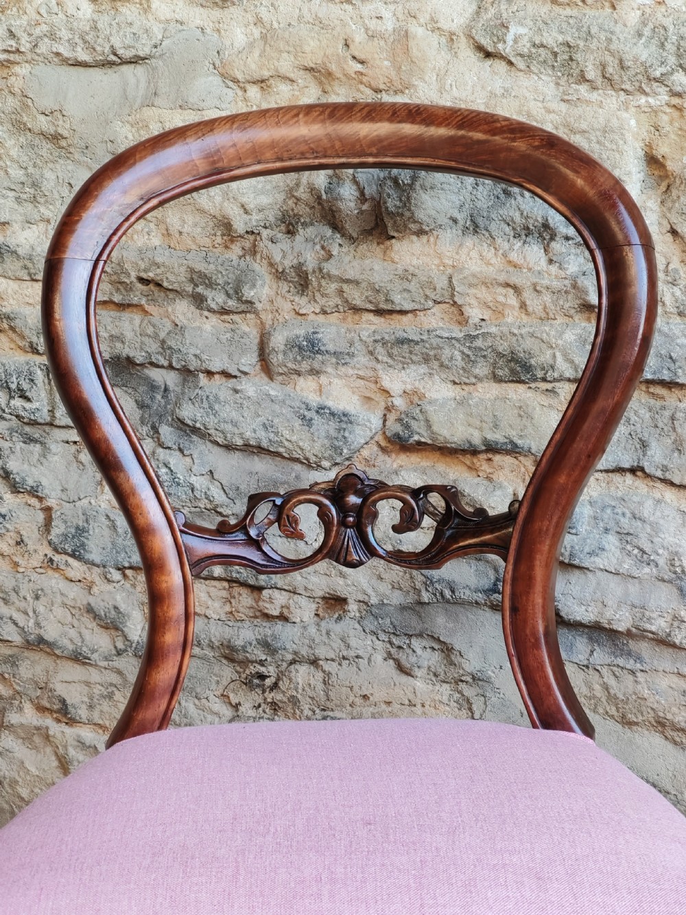 A set of four late Victorian walnut dining chairs featuring balloon backs, carved central splats, cabriole front legs, and pink upholstered seats. View V