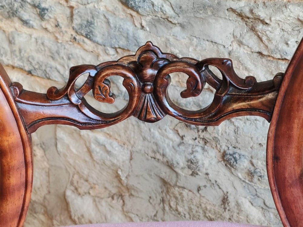 A set of four late Victorian walnut dining chairs featuring balloon backs, carved central splats, cabriole front legs, and pink upholstered seats. View VI