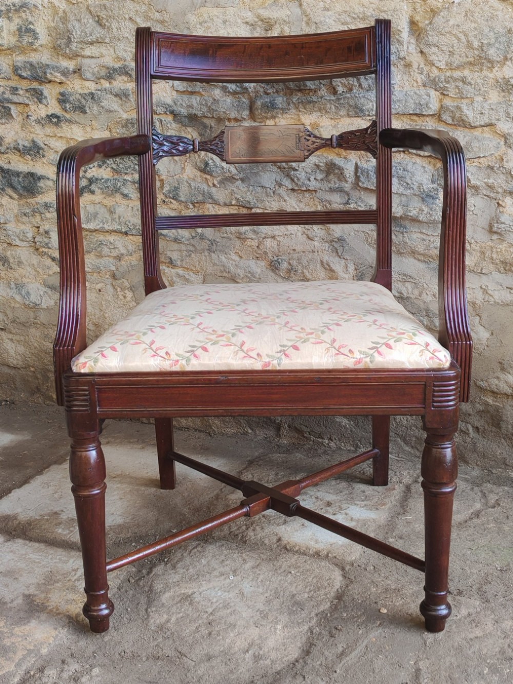 A Georgian mahogany carver armchair featuring reeded arms, a central carved splat, an upholstered seat, turned front legs, and an X-frame stretcher.
