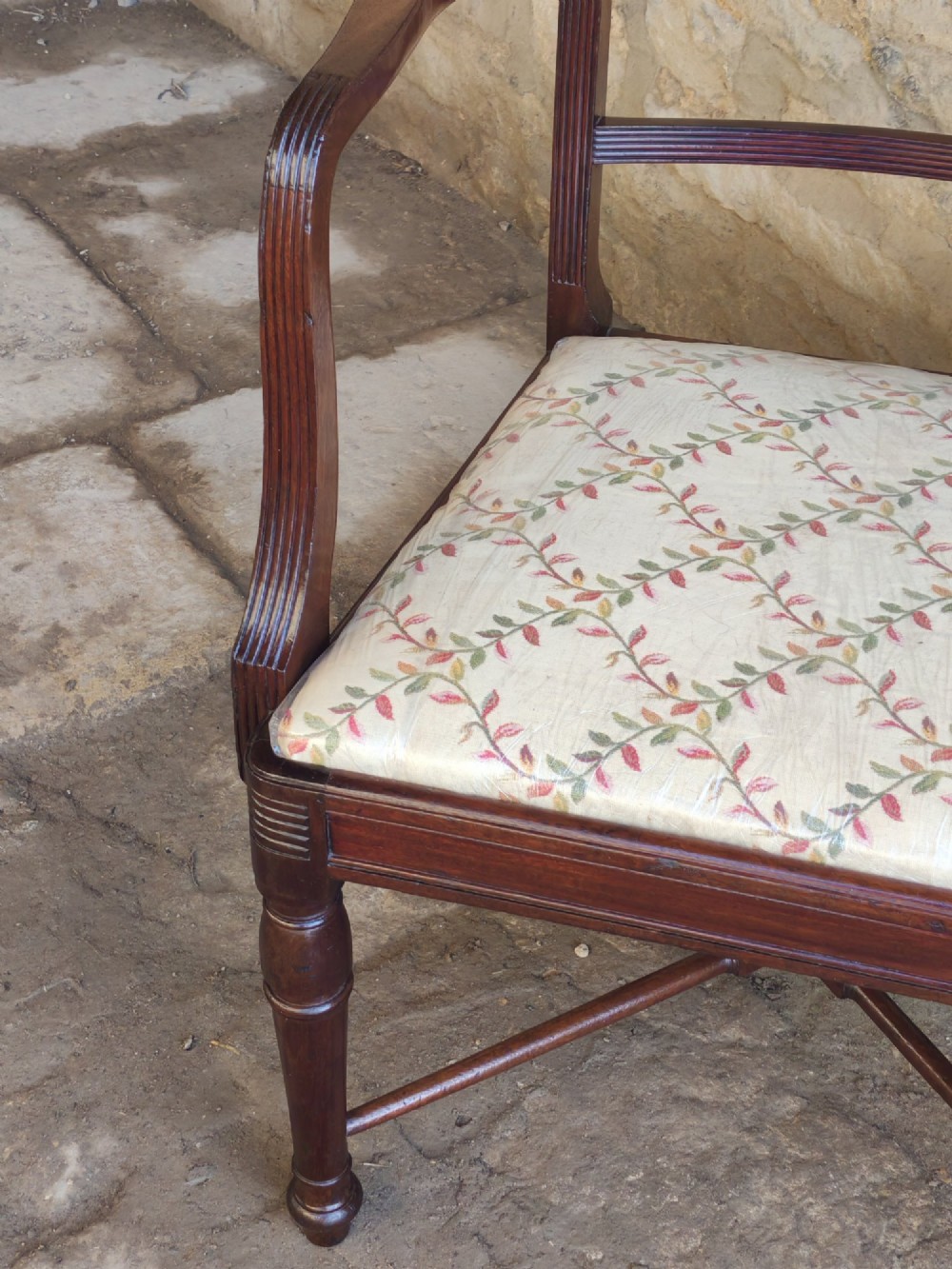 A Georgian mahogany carver armchair featuring reeded arms, a central carved splat, an upholstered seat, turned front legs, and an X-frame stretcher. View V