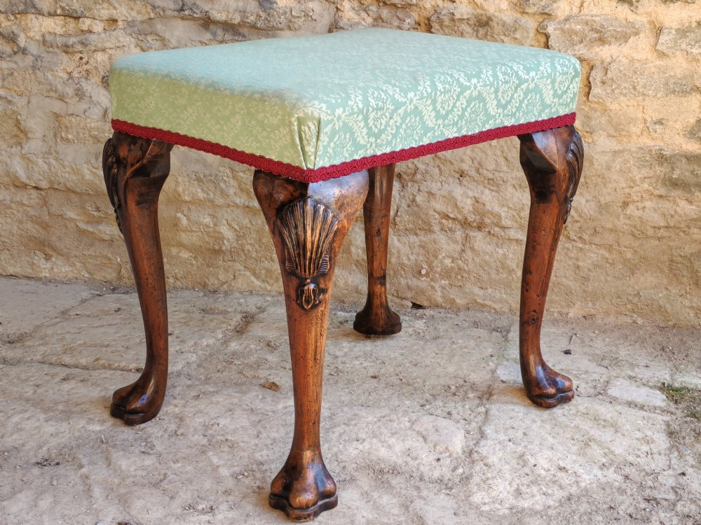 A rectangular 19th-century walnut stool featuring cabriole legs with carved shell details and a light green patterned fabric seat edged with red braid trim.