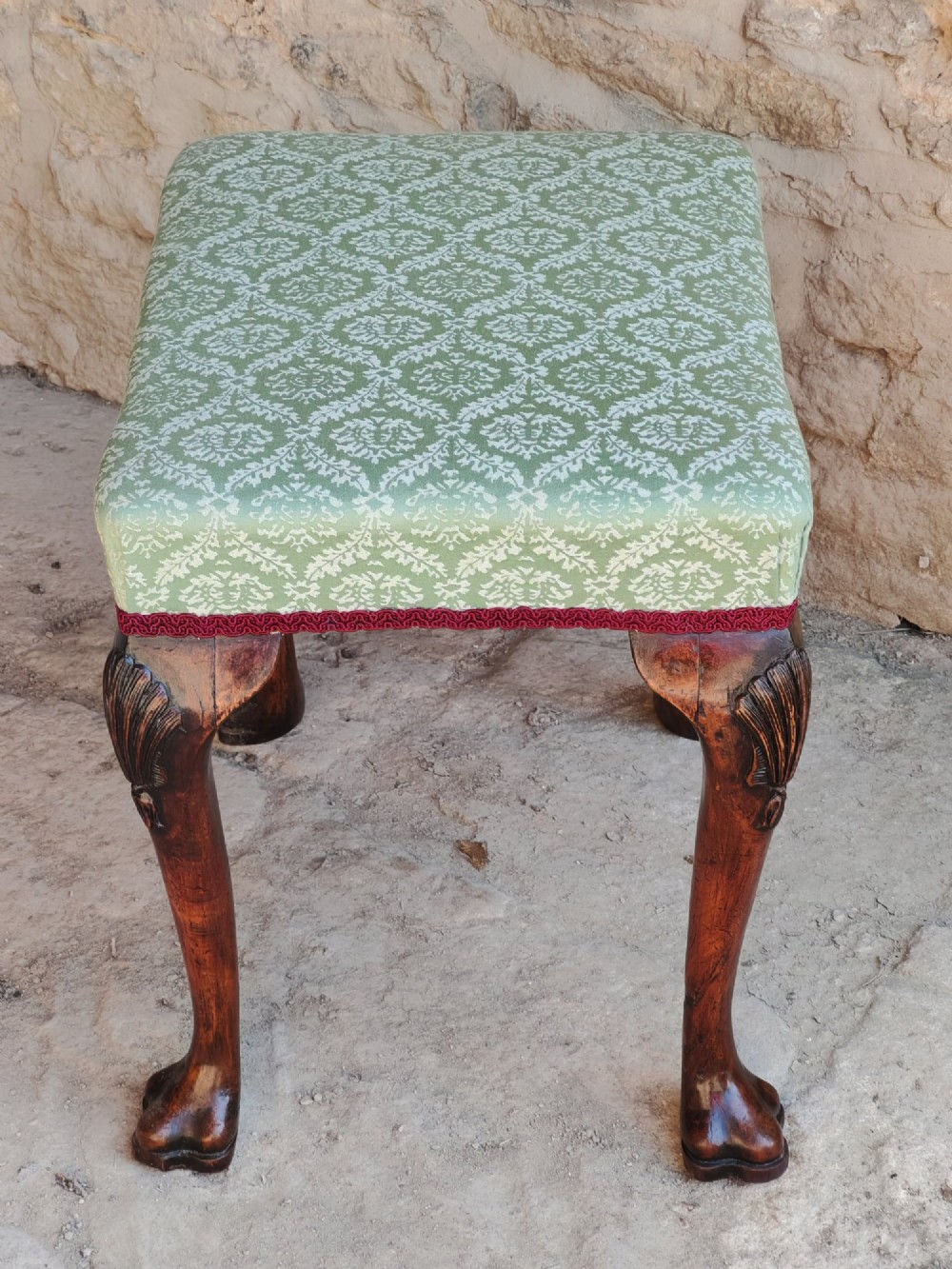 A rectangular 19th-century walnut stool featuring cabriole legs with carved shell details and a light green patterned fabric seat edged with red braid trim. View III