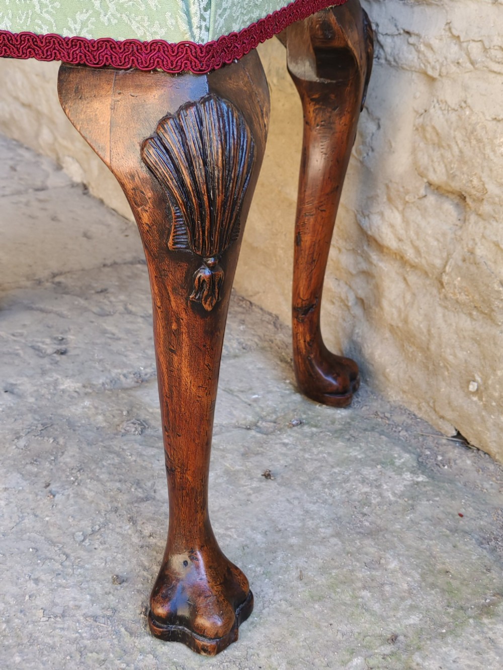 A rectangular 19th-century walnut stool featuring cabriole legs with carved shell details and a light green patterned fabric seat edged with red braid trim. View IV