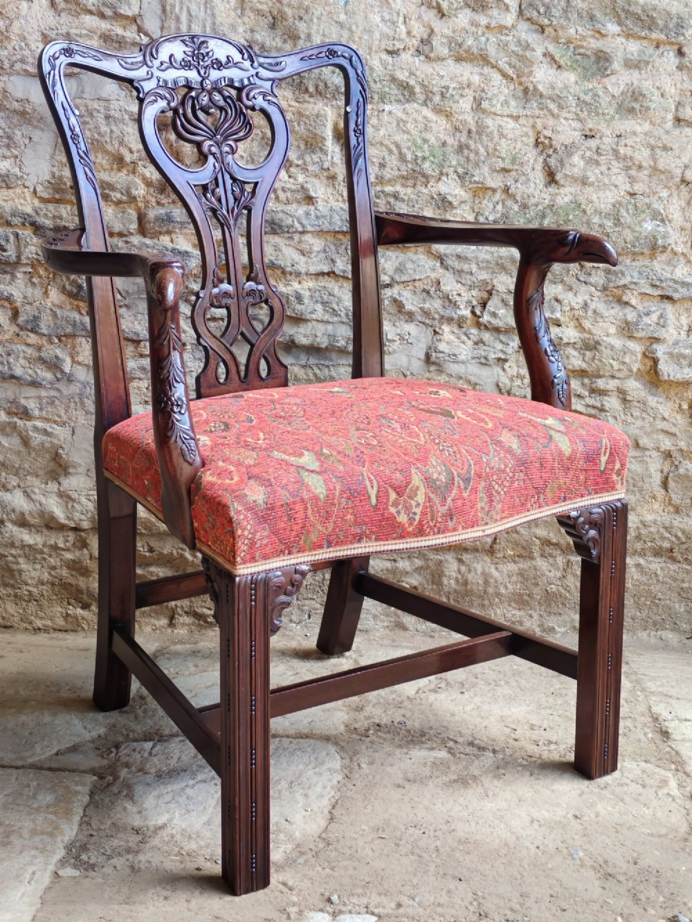 An antique dark mahogany carver armchair with a carved pierced splat back, eagle head armrests, patterned red upholstered seat, and square legs with an H-stretcher.